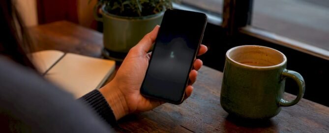Hand holding smartphone near coffee cup